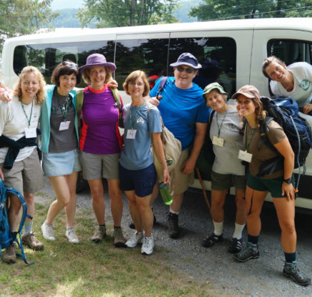 Camp alum standing outside a van in hiking clothes.