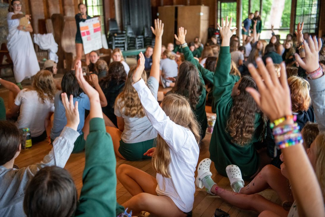 Campers raising their hands in an assembly.