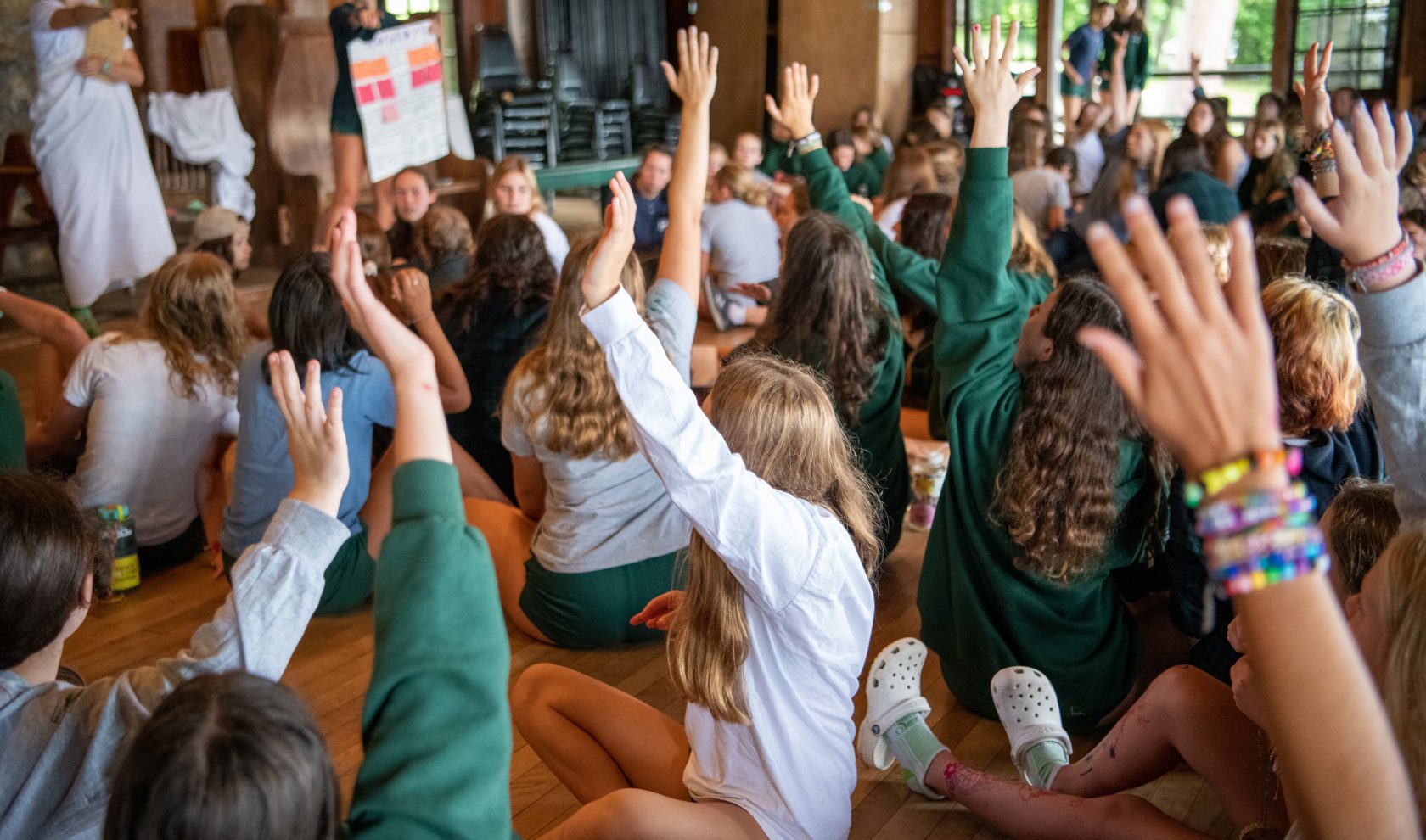 Campers raising their hands in an assembly.