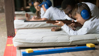 A camper aims a rifle with the guidance of a counselor.