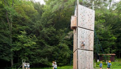 Campers climbing a rock climbing wall outside.