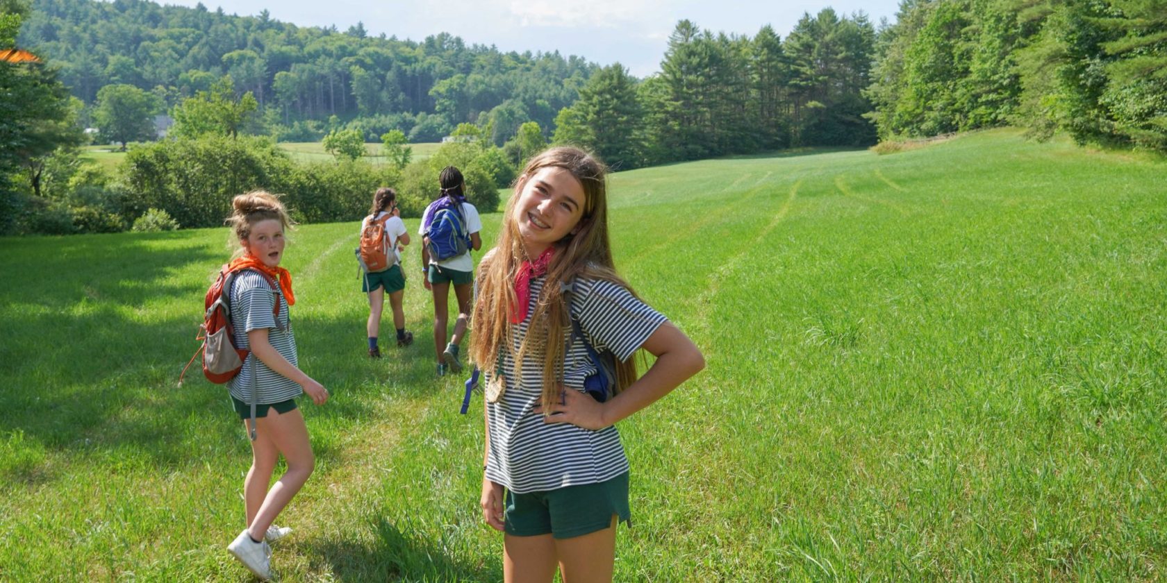 A smiling Hiver with a small camper group in a grassy field on a hike.