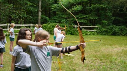 A camper learning how to shoot a bow and arrow.