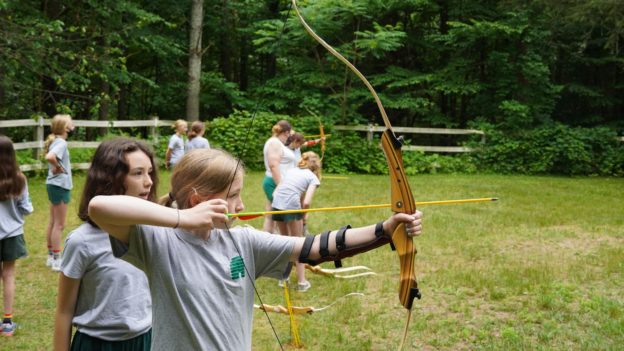 A camper learning how to shoot a bow and arrow.