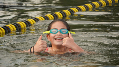 A camper swimming and giving the thumbs up sign.