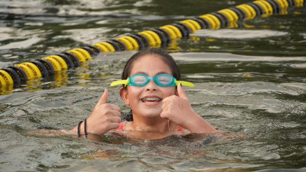 A camper swimming and giving the thumbs up sign.