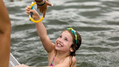 A young girl swimming and reaching out her hand.