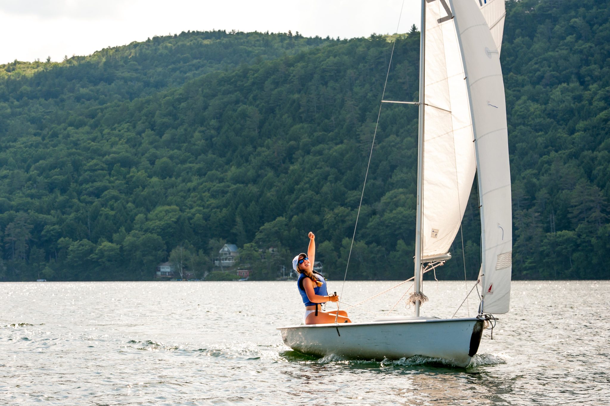 An Aloha camper with their fist in the air as they solo a sailboat on the lake.