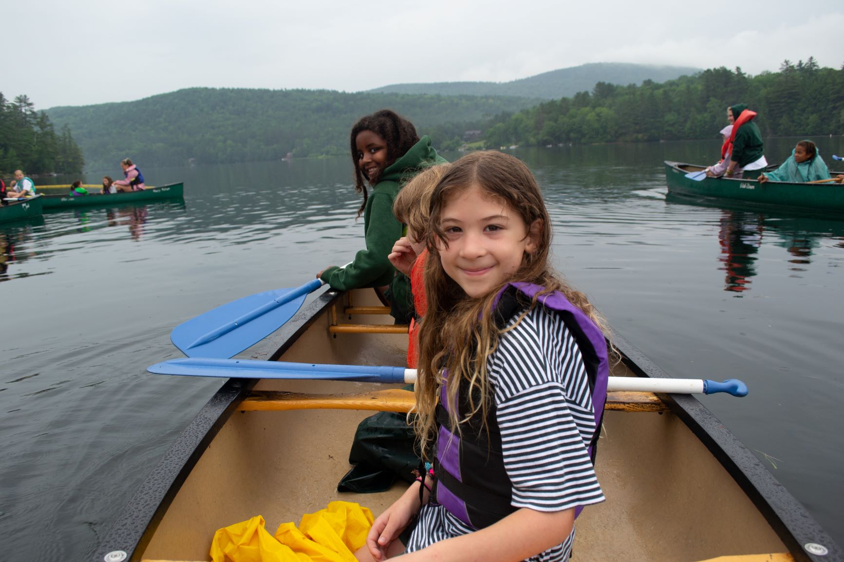 Three campers in a canoe smiling on the lake.