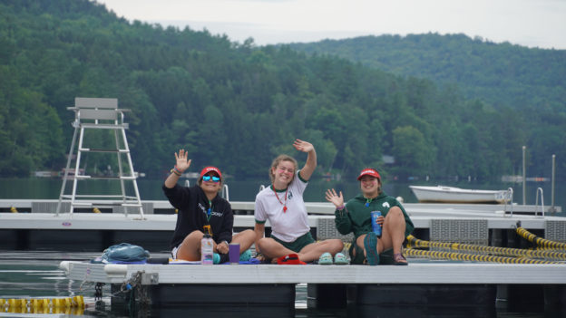 Three Hive counselors waving from a dock on the water.