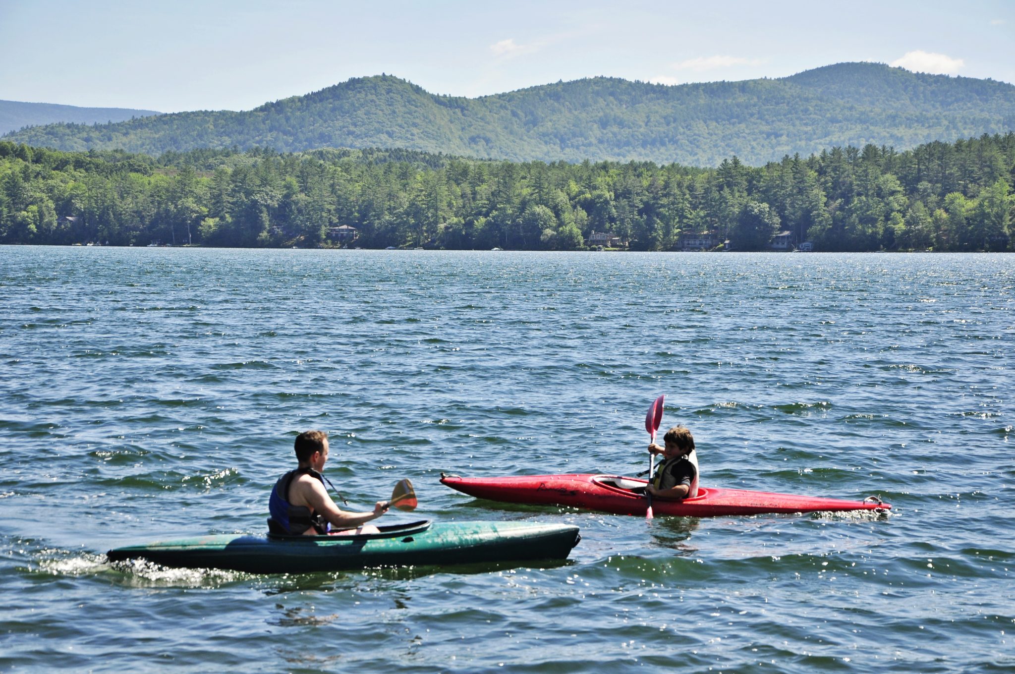 Two people in kayaks out on the lake with the green mountains in the background.
