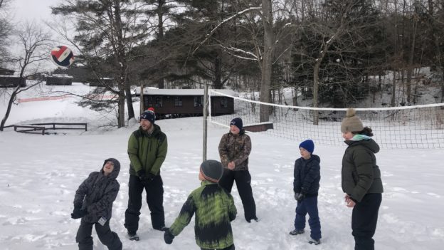 Campers playing volleyball in a court covered in snow.