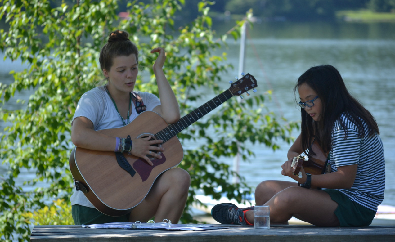 A Hive counselor helping their camper learn to play guitar.