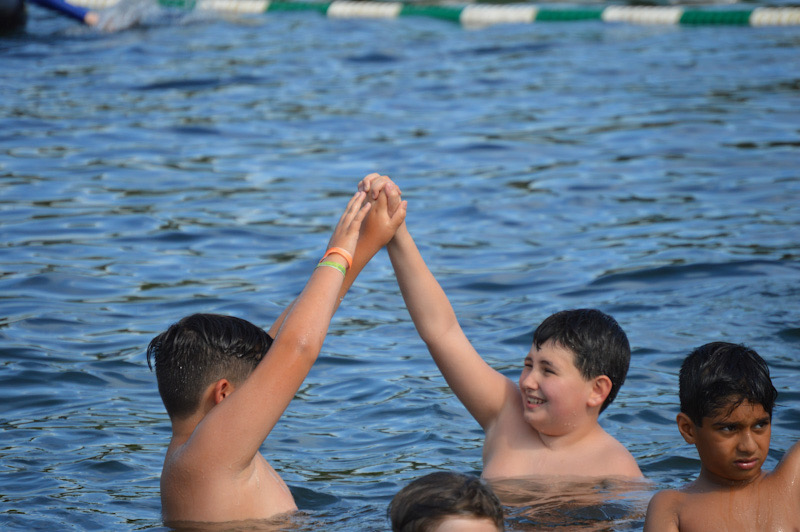 Two Lanakila campers smiling in the lake and making an archway with their arms.