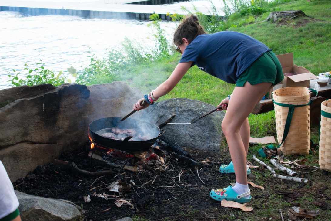 A camper cooking over an open flame by a lake.