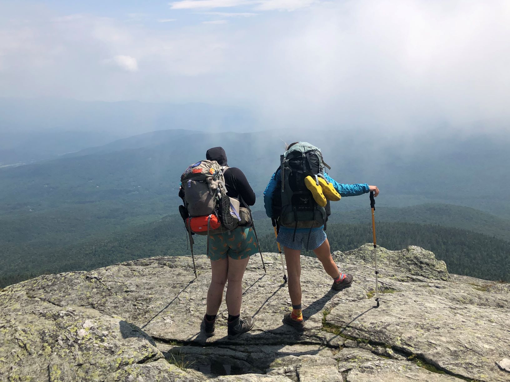 Two hikers on top of a mountain facing out.