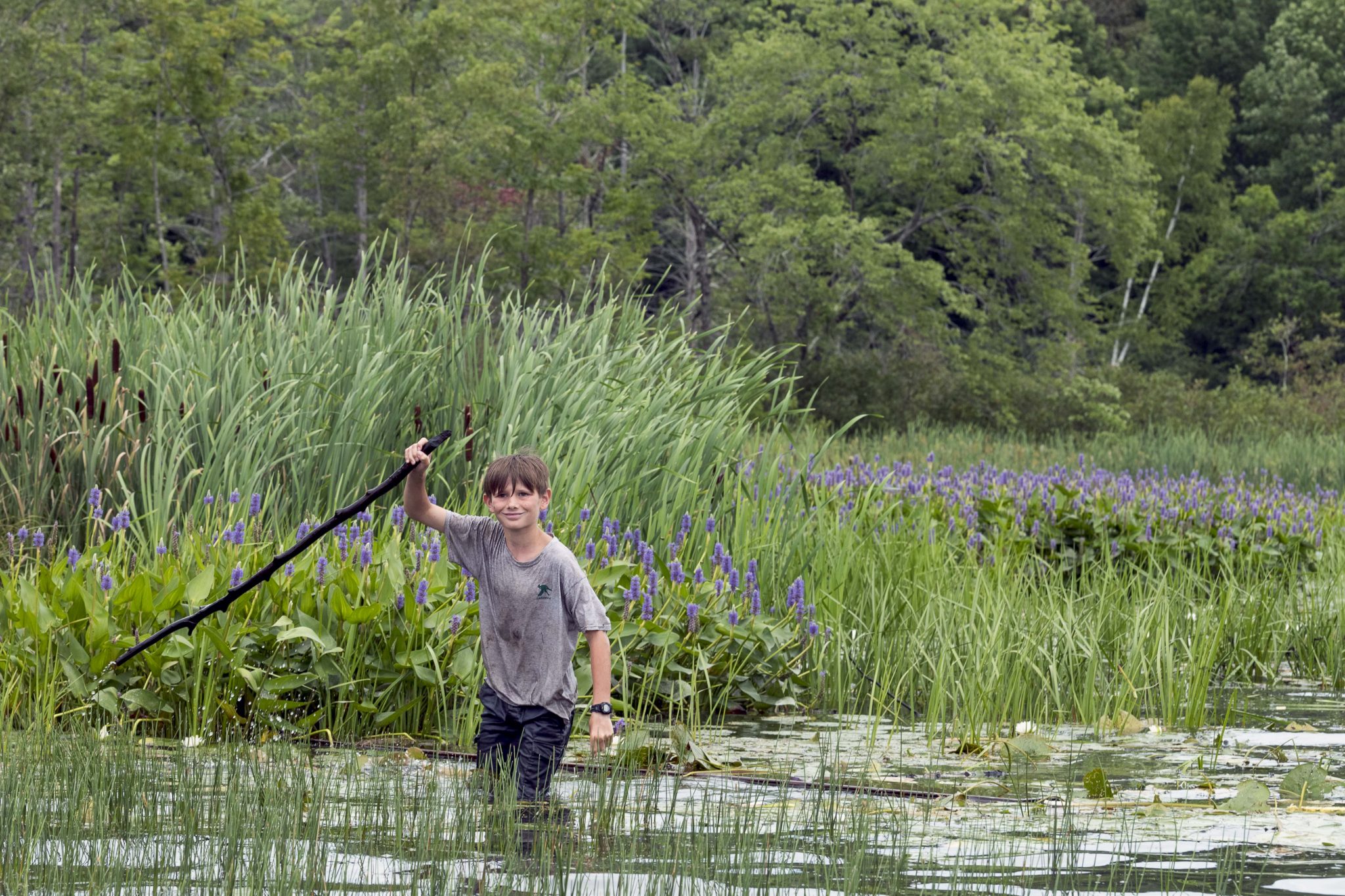 A Lanakila camper walking through the swamp holding a walking stick.