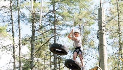 A camper doing a high ropes course moving across a series of hanging tires.