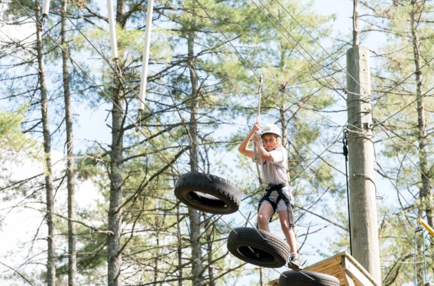 A camper doing a high ropes course moving across a series of hanging tires.