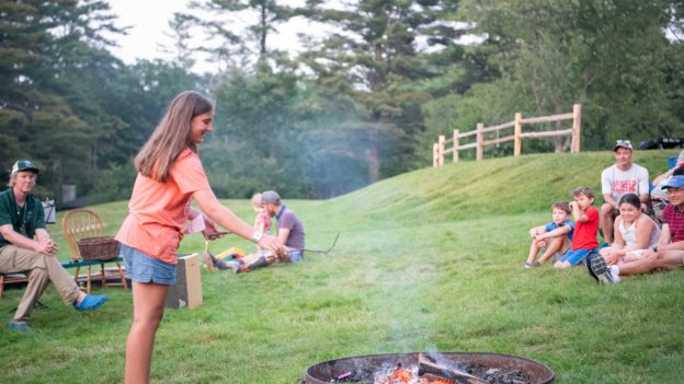 A camper throwing a stick into a firepit.