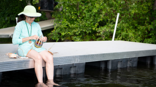 A woman weaving a basket while sitting on a dock.