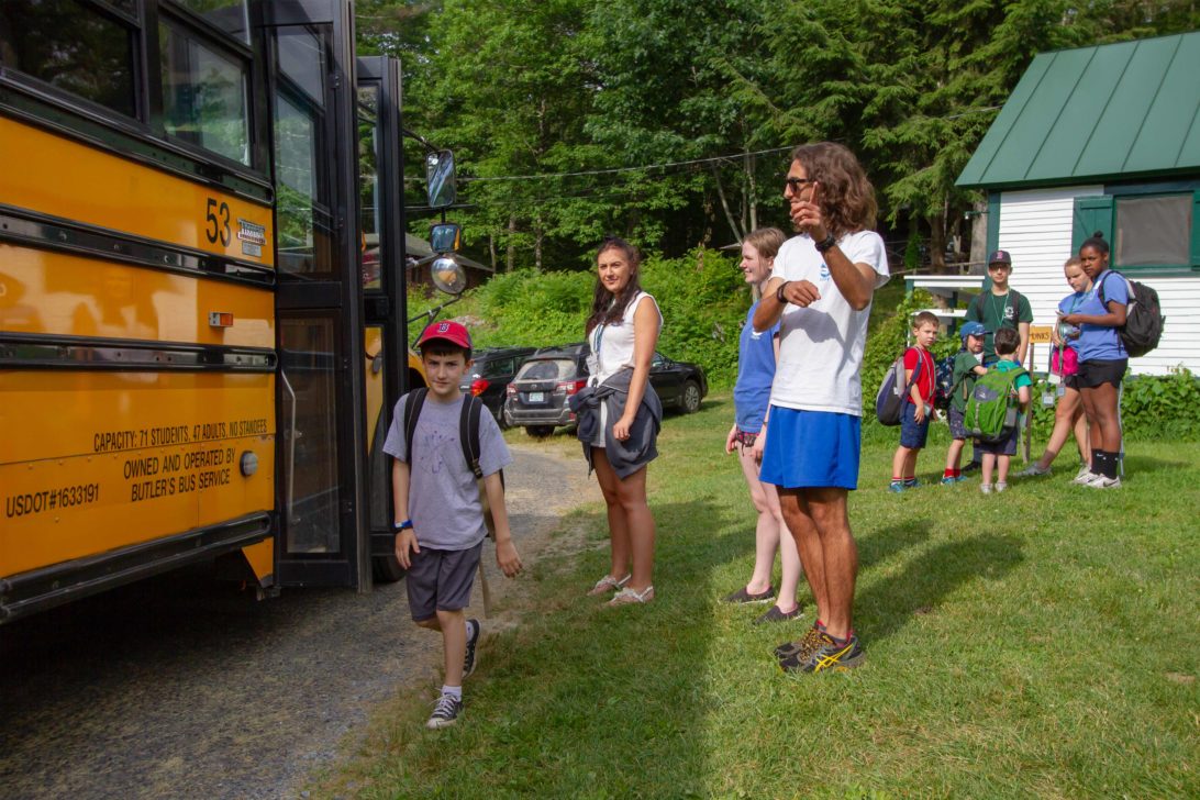 Young campers being dropped off from a yellow school bus.