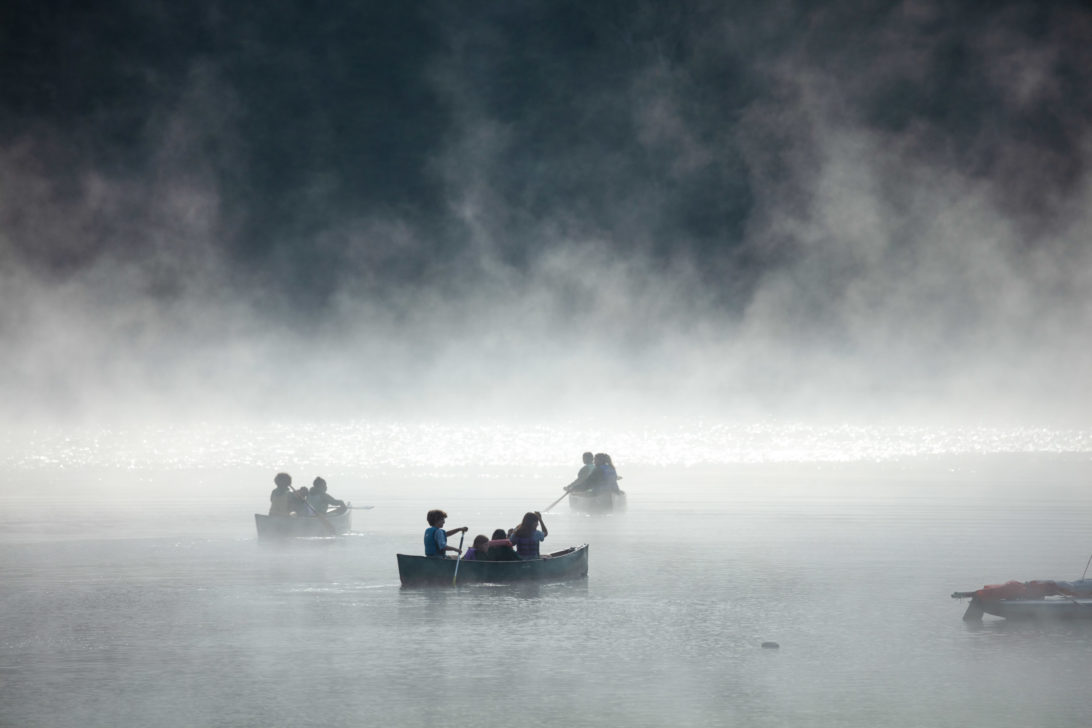 A lake shrouded in mist with people on canoes.