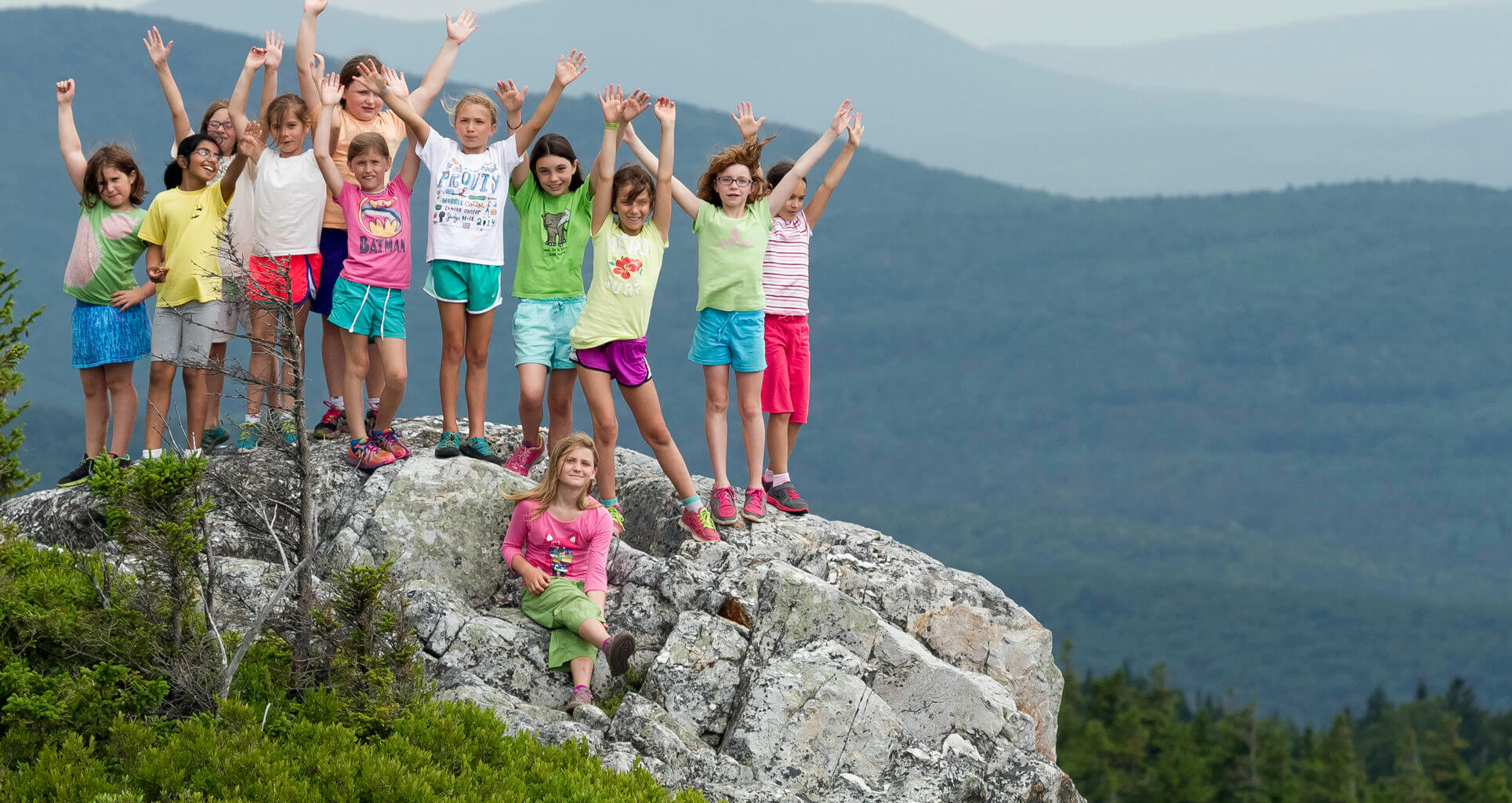 A group of young children with their hands in the air on the summit of a mountain.
