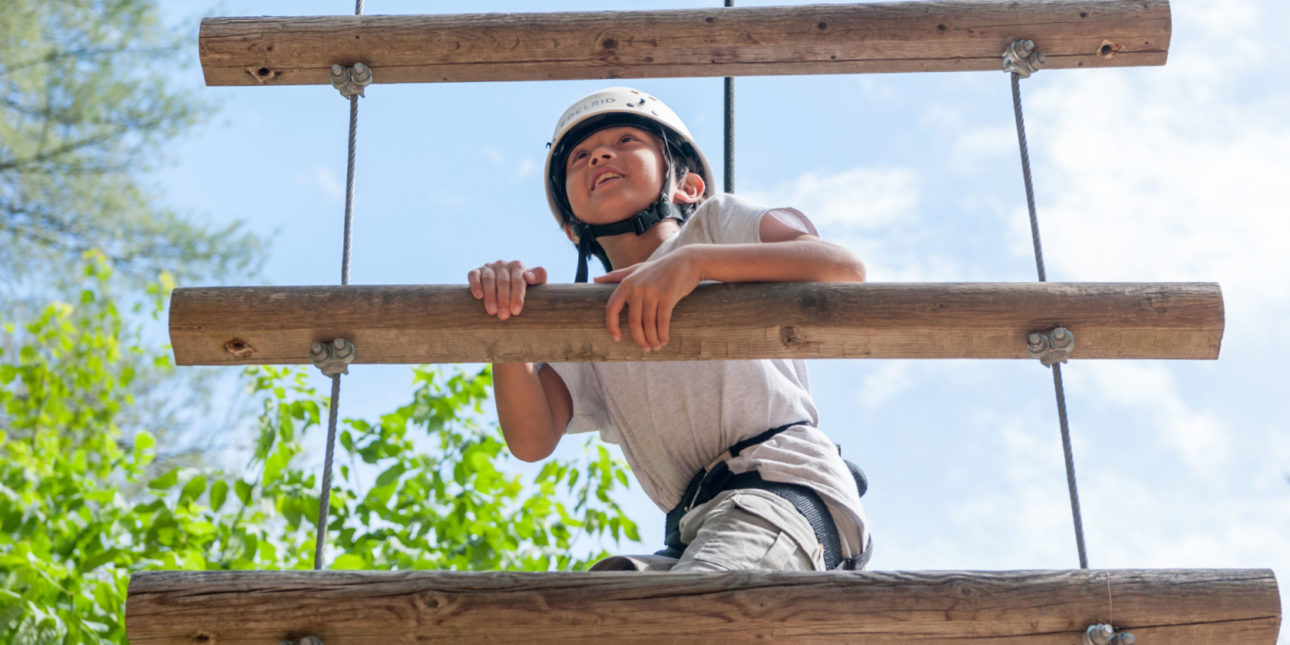 A child wearing a helmet climbing up a ladder on the ropes course.
