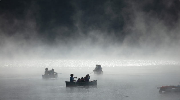 A black and white view of people canoeing on a lake.