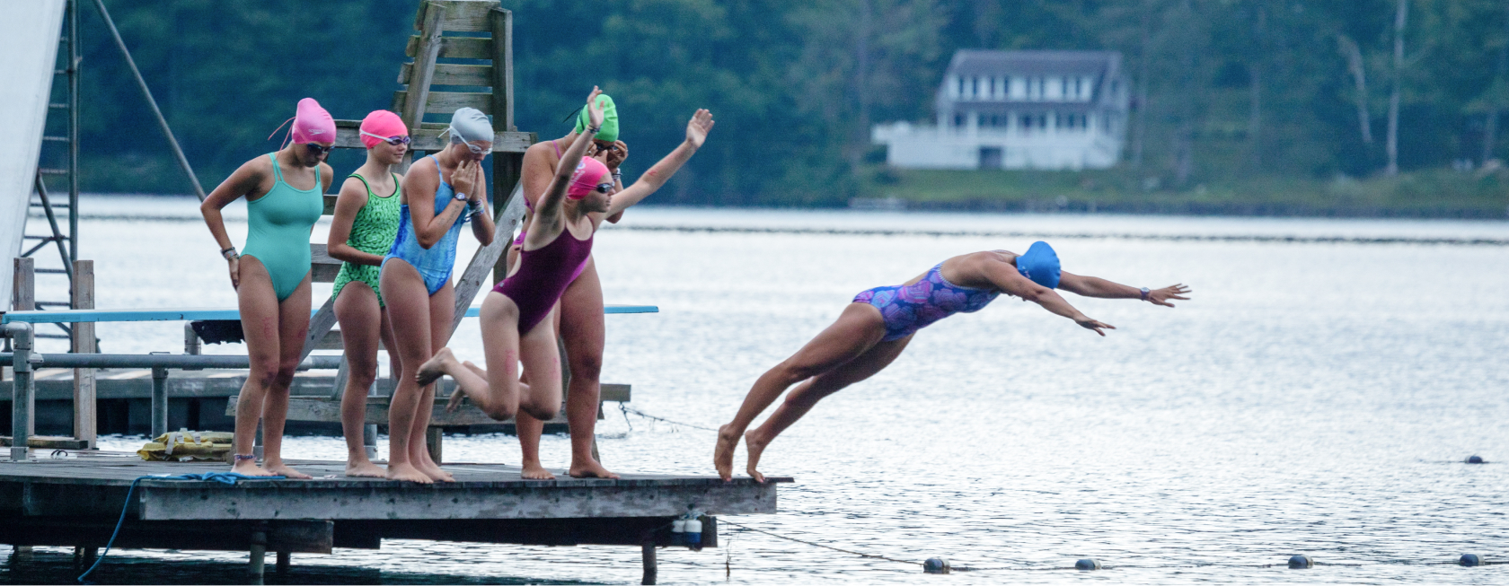 Campers in bathing suits, jumping into a lake from a dock.