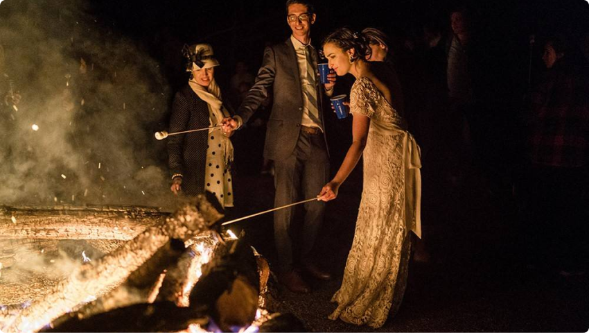 A bride toasting a marshmallow at a campfire.