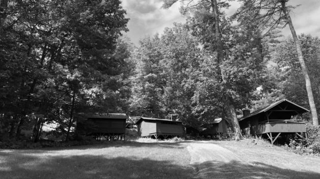 A black and white view of open air cabins surrounded by trees.