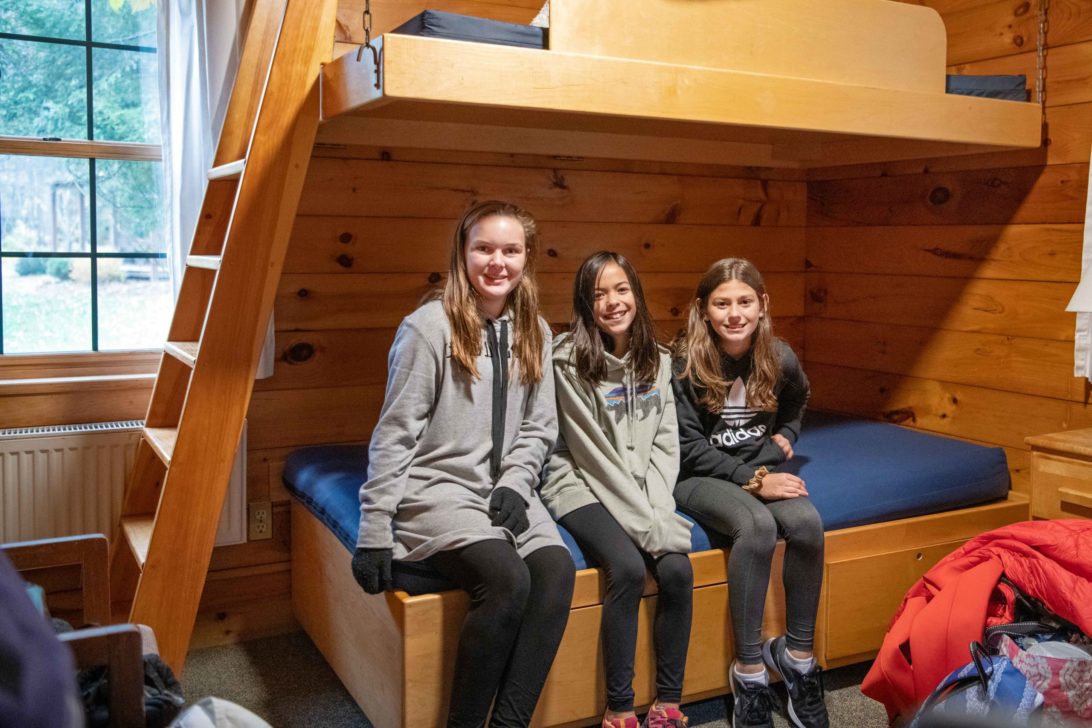 Three girls sitting on a bed in one of the Hulbert cabins.
