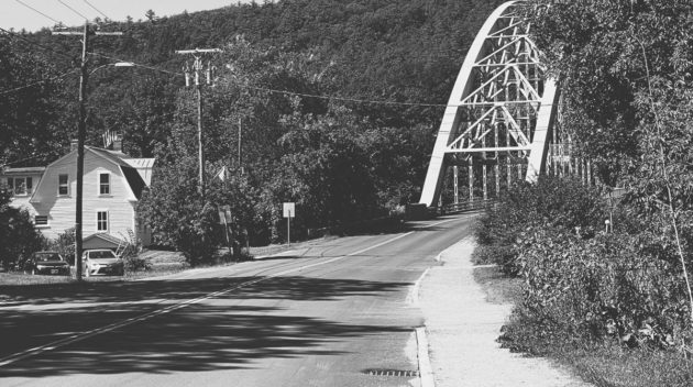 A black and white view of a road leading to a bridge.
