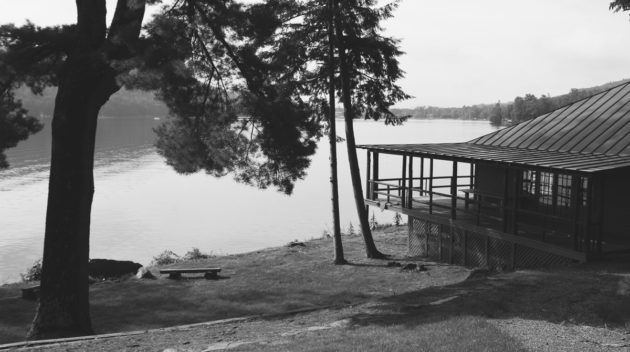A black and white view of a lodge overlooking a lake.