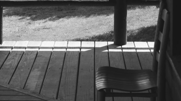 A black and white view of a chair on a porch.
