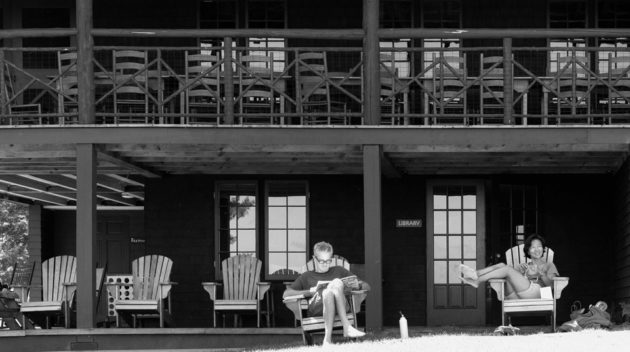 A black and white view of two campers relaxing on lawn chairs.