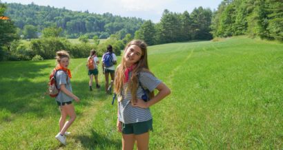 A smiling Hiver with a small camper group in a grassy field on a hike.