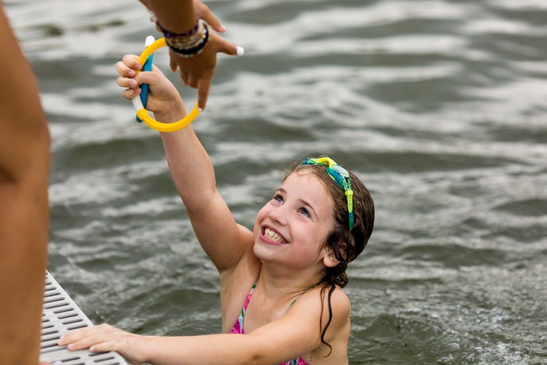 A young girl swimming and reaching out her hand.