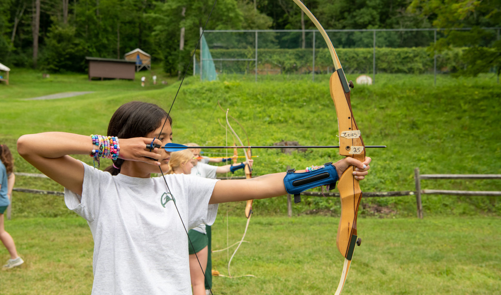 Camper drawing back a bow to shot an arrow at archery.
