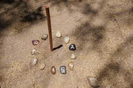 A sundial composed of a stick casting a shadow in a circle of rocks.