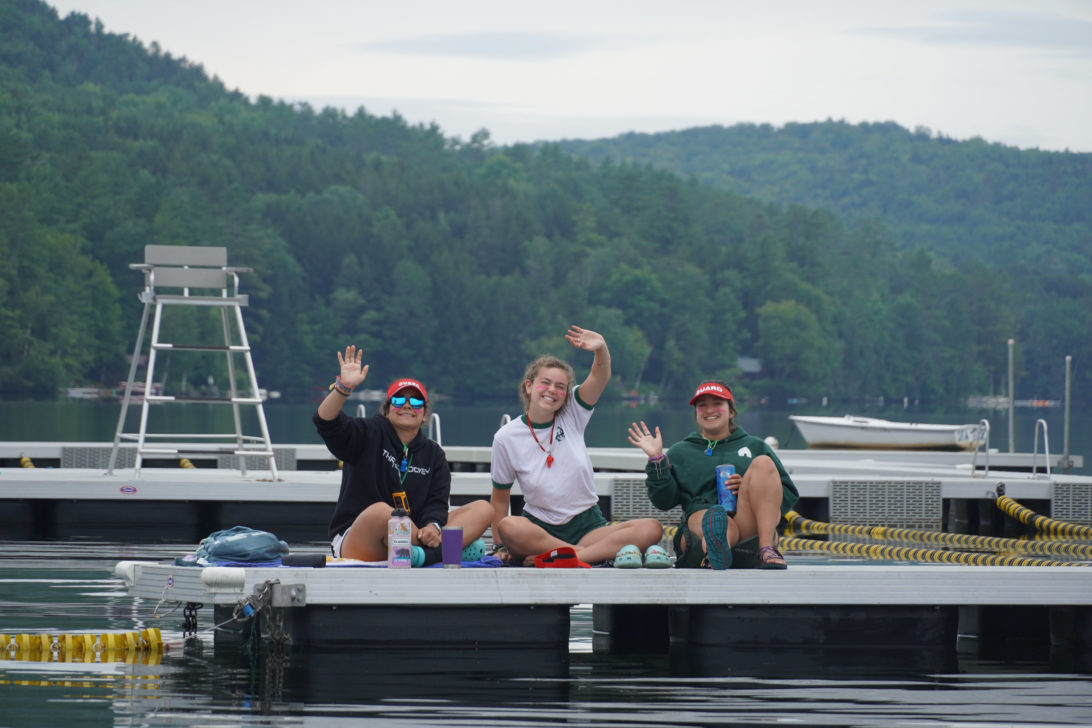 Three Hive counselors waving from a dock on the water.