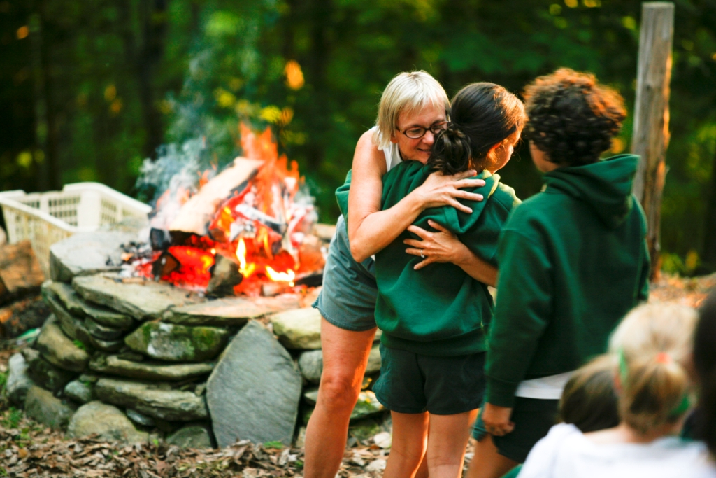 Former Hive Director Kathy Plunkett giving a Hiver a hug in front of camp fire.