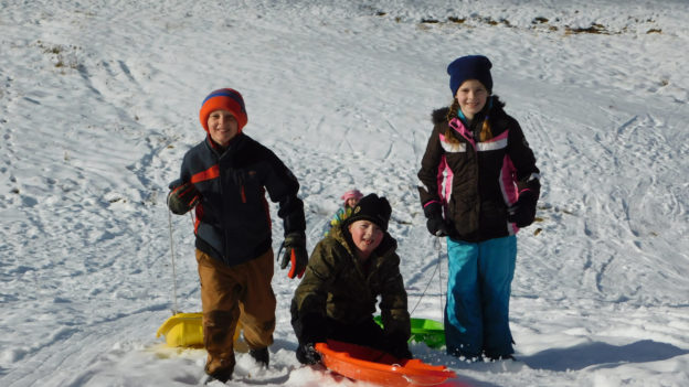A group of kids with sleds smiling on a snowy hill.