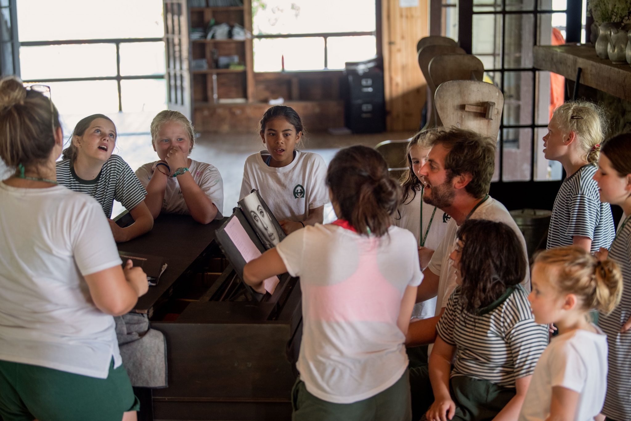 A group of Hivers singing around a counselor playing the piano.