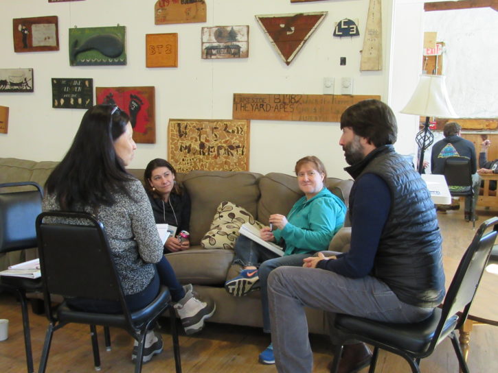 A group of four people sitting on chairs and a couch talking.