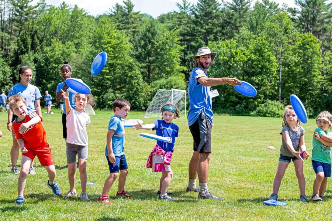 Young campers and a counselor throwing blue frisbees.