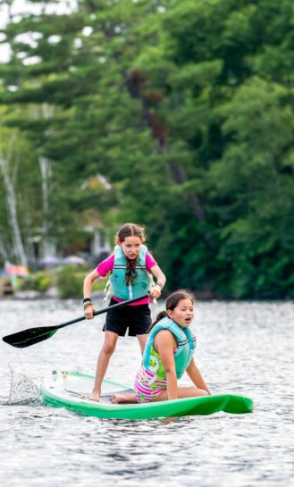 Two young girls paddle boarding.