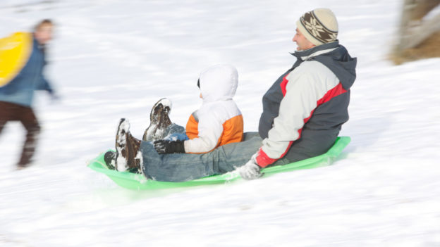 A father and child sledding down a hill together.